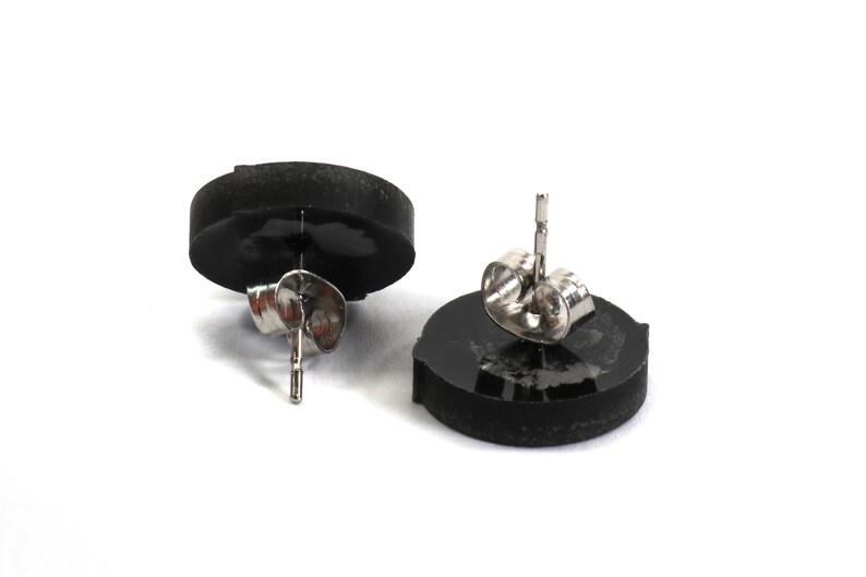 May include: A pair of black stud earrings with silver posts and backs. The earrings are round and have a smooth, polished finish.