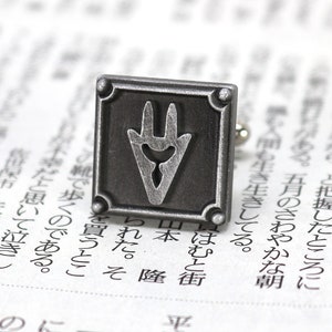 May include: Silver cufflinks with a square design featuring a stylized, three-pronged symbol in the center.