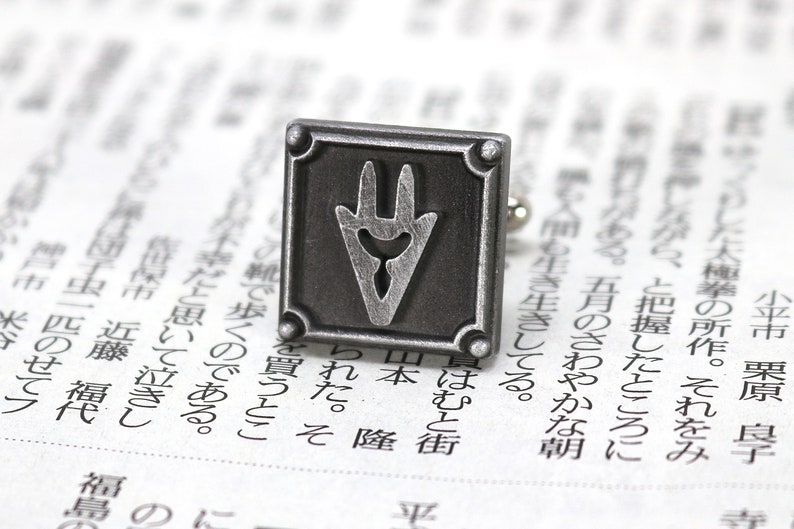 May include: Silver cufflinks with a square design featuring a stylized, three-pronged symbol in the center.