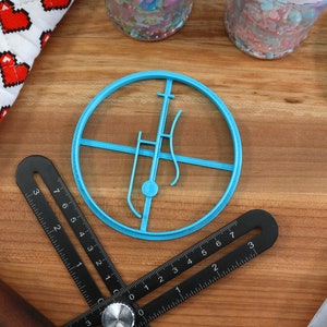 May include: A blue plastic cookie cutter shaped like a musical note with a circle around it. The cutter is on a wooden surface with a black ruler and a blue spatula.