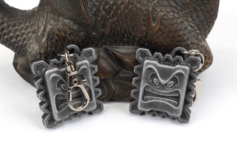 May include: Two silver-colored keychains with a detailed, angry face design. The keychains are attached to a silver keyring.