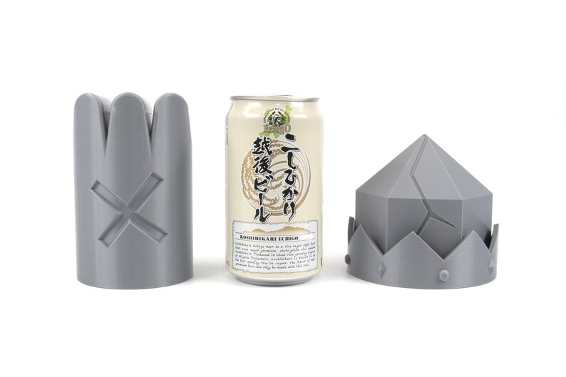 May include: Three gray 3D printed objects: a crown, a cylinder with a cross, and a can of beer with Japanese text that reads "Koshihikari Ale Echigo" and "二割三分".