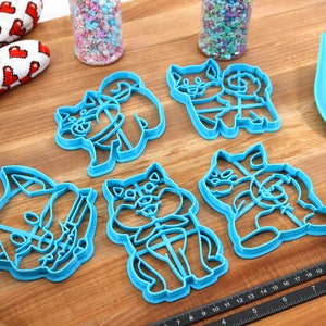May include: Set of five blue plastic cookie cutters shaped like dogs. The cutters are on a wooden surface.