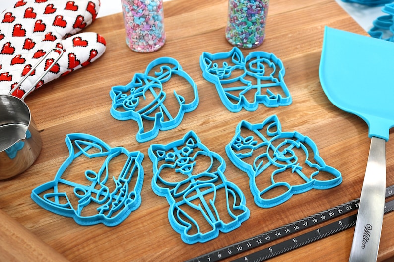 May include: Set of five blue plastic cookie cutters shaped like dogs. The cutters are on a wooden surface.