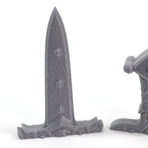 May include: Two gray 3D printed fantasy style daggers with intricate designs. The daggers have a sharp point and a curved handle.