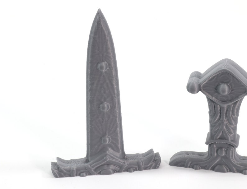 May include: Two gray 3D printed fantasy style daggers with intricate designs. The daggers have a sharp point and a curved handle.