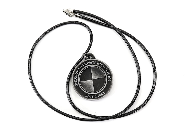 May include: A black cord necklace with a silver pendant featuring the Gekkoukan Private High School logo. The logo is a circle with a black and white quartered design and the text "Gekkoukan Private High School Since 1982".