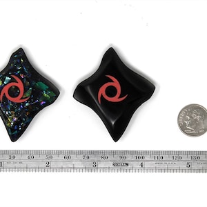 May include: Two black star-shaped ninja throwing stars with a red swirl design. One star is made of iridescent glass and the other is solid black.