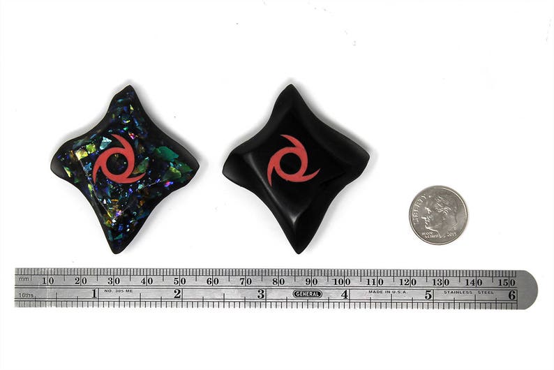 May include: Two black star-shaped ninja throwing stars with a red swirl design. One star is made of iridescent glass and the other is solid black.