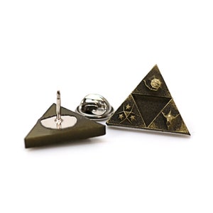 May include: A gold-toned triangular pin with a design of a stylized triangle with three symbols inside. The pin is on a white background.