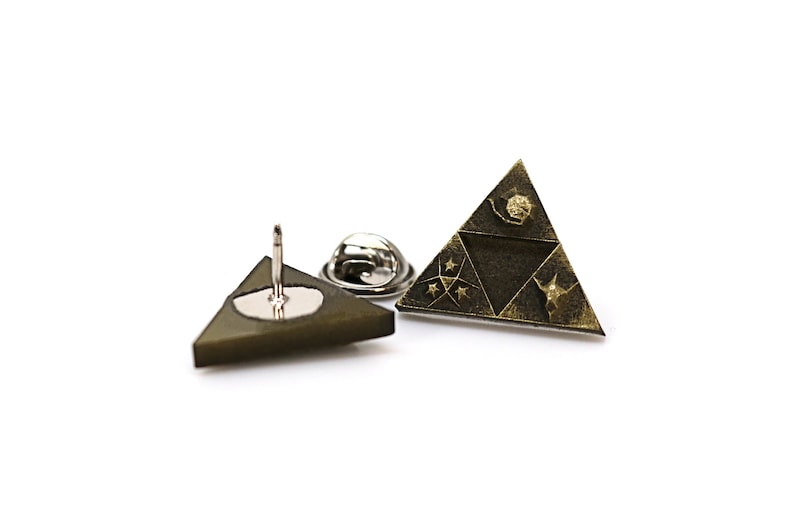 May include: A gold-toned triangular pin with a design of a stylized triangle with three symbols inside. The pin is on a white background.