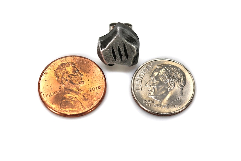 May include: A silver-colored metal earring shaped like a knight's helmet. The earring is shown next to two US coins, a penny and a dime, to show its size.