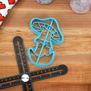 May include: A blue plastic mushroom-shaped cookie cutter on a wooden surface.