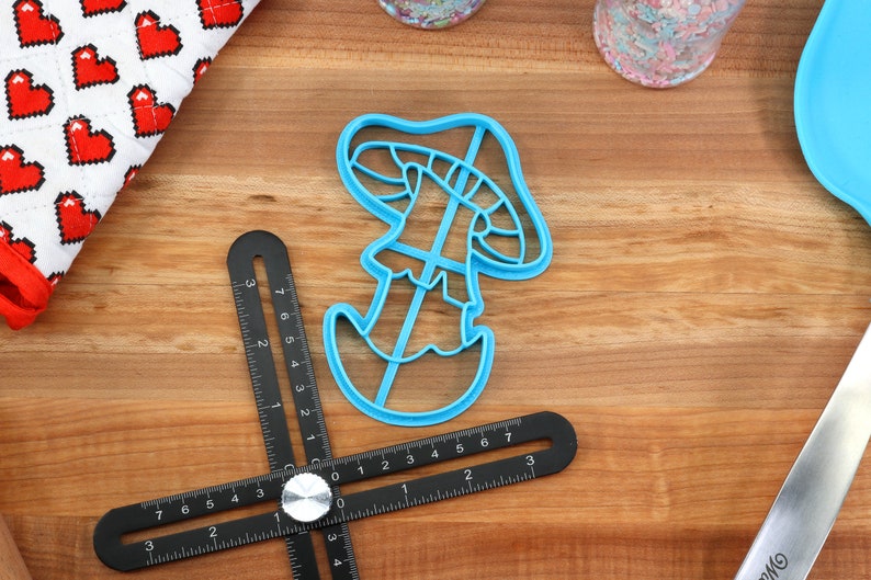 May include: A blue plastic mushroom-shaped cookie cutter on a wooden surface.