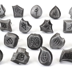 Puede incluir: Una colecci&oacute;n de veintiuna piezas de juego de metal gris desgastado con s&iacute;mbolos grabados. Las piezas tienen formas variadas, incluyendo cuadrados, c&iacute;rculos y formas irregulares. Cada pieza presenta un dise&ntilde;o grabado &uacute;nico.