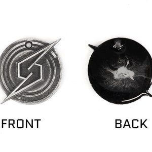 May include: A silver-colored metal pendant with a stylized 'S' logo on the front and a black background with a silver-colored design on the back.