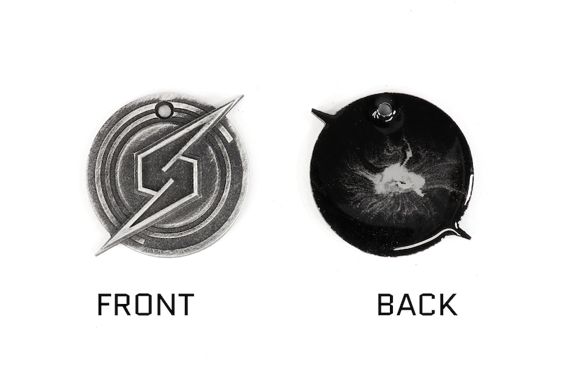 May include: A silver-colored metal pendant with a stylized 'S' logo on the front and a black background with a silver-colored design on the back.