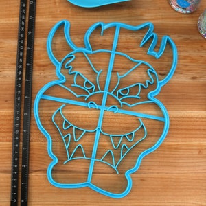 Op de afbeelding: Blauwe plastic koekjesvormer in de vorm van een cartoon monster gezicht met een wijd open mond en scherpe tanden. De vormer is verdeeld in vier secties door lijnen.