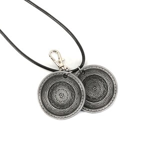 May include: A black cord necklace with a silver clasp and two silver circular pendants. Each pendant features a detailed, intricate design.