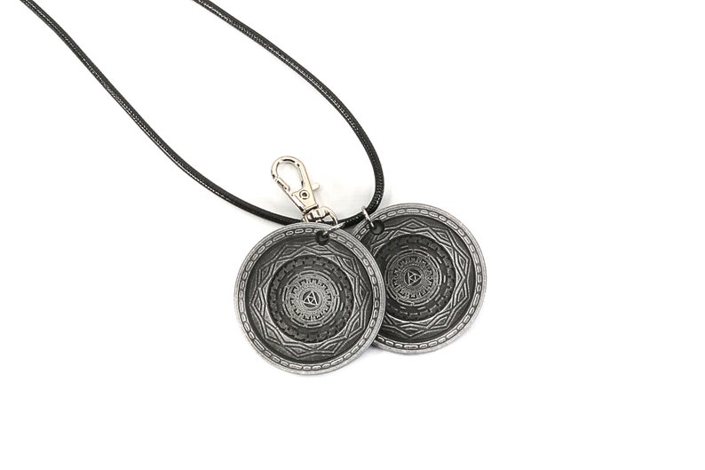 May include: A black cord necklace with a silver clasp and two silver circular pendants. Each pendant features a detailed, intricate design.