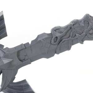 May include: A gray 3D printed model of a sword with a detailed design. The sword has a triangular blade with a textured surface and a handle with a wing-like design.