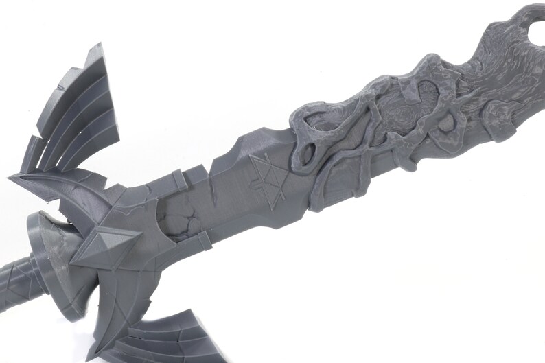 May include: A gray 3D printed model of a sword with a detailed design. The sword has a triangular blade with a textured surface and a handle with a wing-like design.