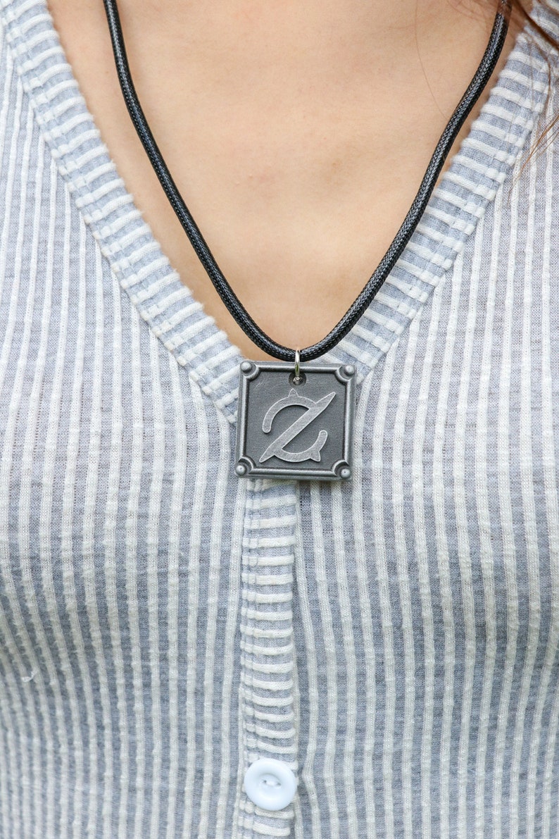 Pu&ograve; includere: Una collana con cordoncino in pelle nera con un ciondolo quadrato in argento con una lettera 'Z' stilizzata.