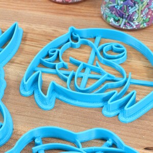 Puede incluir: Un juego de cortadores de galletas de pl&aacute;stico azul con forma de personajes de dibujos animados. Los cortadores est&aacute;n sobre una superficie de madera.