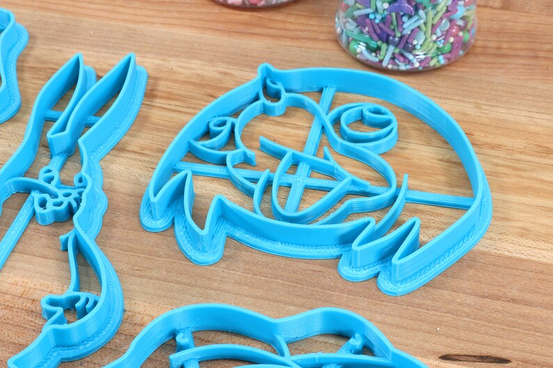 Puede incluir: Un juego de cortadores de galletas de pl&aacute;stico azul con forma de personajes de dibujos animados. Los cortadores est&aacute;n sobre una superficie de madera.