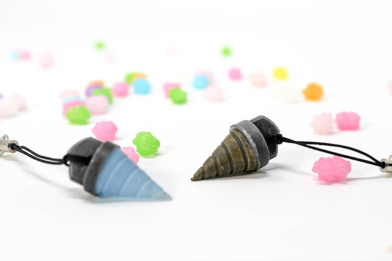 May include: Two small, detailed drill bit charms with black cords. One charm is blue and the other is brown and silver.