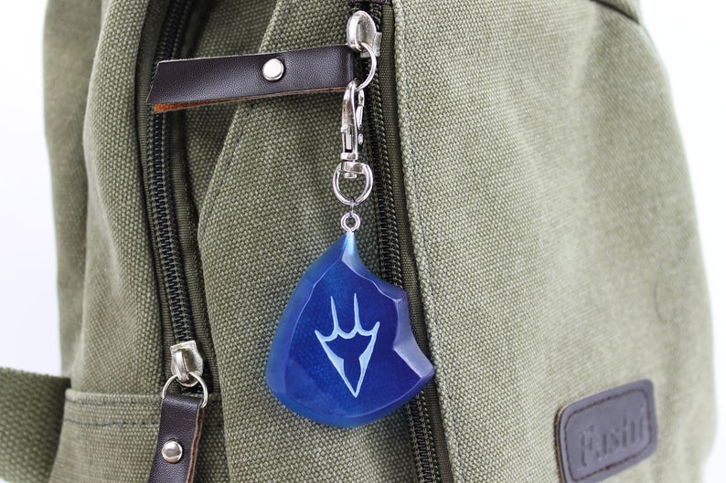 May include: A blue and silver keychain with a stylized hand design. The keychain is attached to a green canvas bag.