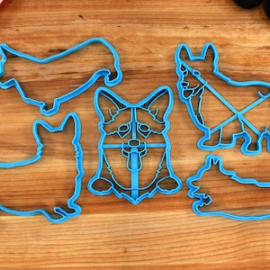 May include: A set of five blue plastic cookie cutters shaped like different breeds of dogs. The cutters are on a wooden surface.