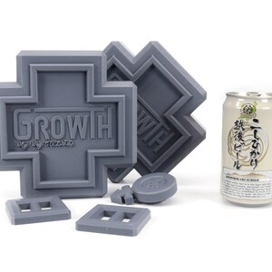 May include: A set of gray plastic building blocks with the word "GROWTH" printed on one of the blocks. The blocks are shaped like crosses and squares. A can of beer is also in the image.
