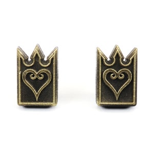 May include: Two bronze-colored rectangular earrings with a crown design at the top and a heart in the center. The earrings are set against a white background.