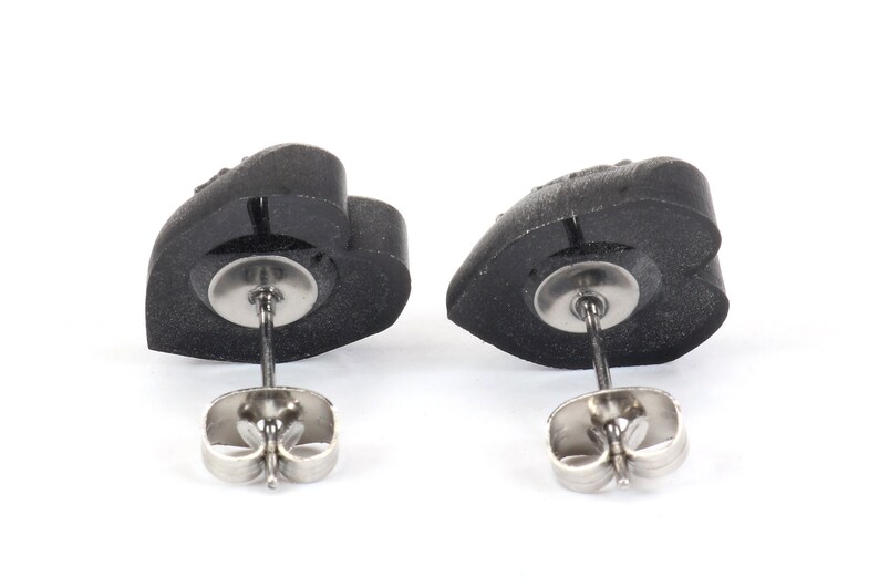 May include: A pair of black heart-shaped stud earrings with silver posts and butterfly backs.