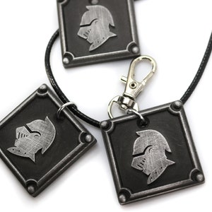 May include: Three silver-toned metal pendants with a knight's helmet design. The pendants are attached to a black cord and a silver-toned metal clasp.