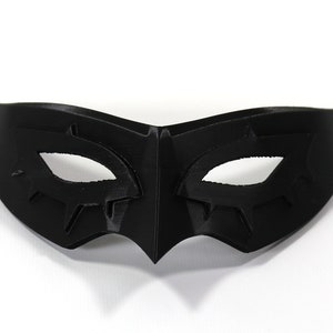 May include: A black masquerade mask with a stylized eye design. The mask is made of a smooth, hard material.