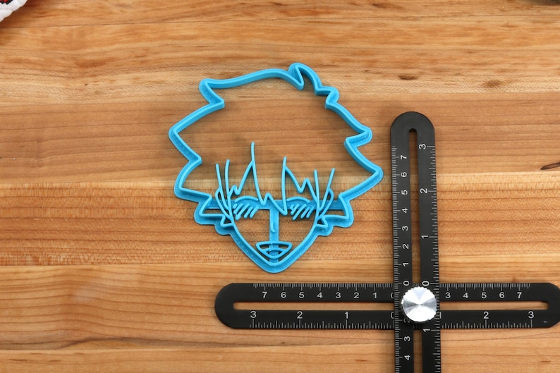 May include: A blue plastic cookie cutter shaped like a cartoon character with spiky hair and sunglasses. The cutter is approximately 2 inches wide.