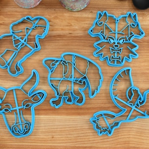 May include: Five blue plastic cookie cutters shaped like a bull, a dragon, a three-headed wolf, a unicorn, and a bird.