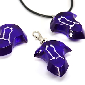 May include: Three blue glass pendants with a white Gemini constellation design. One pendant is on a black cord, one is on a silver chain, and one is on a silver ring.