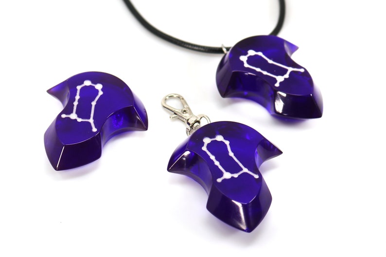 May include: Three blue glass pendants with a white Gemini constellation design. One pendant is on a black cord, one is on a silver chain, and one is on a silver ring.