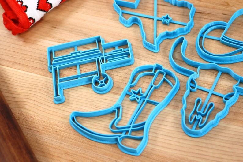 May include: A set of blue plastic cookie cutters shaped like a cowboy boot, a grill, a longhorn skull, a cowboy hat, and the state of Texas.
