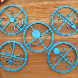 Op de afbeelding: Vijf blauwe plastic koekjesvormen met verschillende ontwerpen. De vormen liggen op een houten oppervlak.