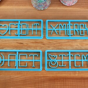 May include: Four blue plastic cookie cutters with different designs. The cutters spell out the words "FIGHT", "MERRY", "ACT", and "ITEM".