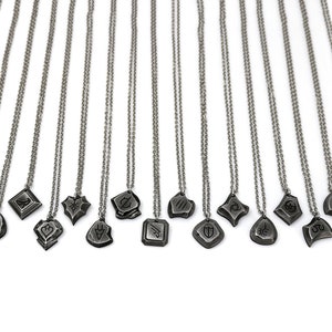 Pode incluir: Um conjunto de 16 colares de prata com diferentes pingentes. Cada pingente apresenta um design &uacute;nico, incluindo formas geom&eacute;tricas, s&iacute;mbolos e padr&otilde;es abstratos. Os colares est&atilde;o todos sobre um fundo branco.