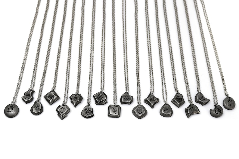 Pode incluir: Um conjunto de 16 colares de prata com diferentes pingentes. Cada pingente apresenta um design &uacute;nico, incluindo formas geom&eacute;tricas, s&iacute;mbolos e padr&otilde;es abstratos. Os colares est&atilde;o todos sobre um fundo branco.