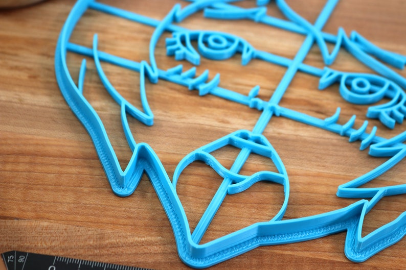 May include: A blue plastic cookie cutter shaped like a cartoon animal face with detailed features, including eyes, nose, and mouth.