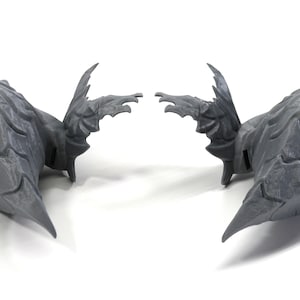 Op de afbeelding: Een paar grijze, 3D-geprinte vleugels met een textuur. De vleugels zijn symmetrisch en hebben een puntige vorm.