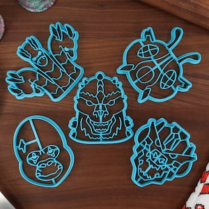 May include: Five blue plastic cookie cutters shaped like different monsters. The cutters are on a wooden surface.