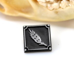 May include: A silver wheat stalk design on a black square metal pin.